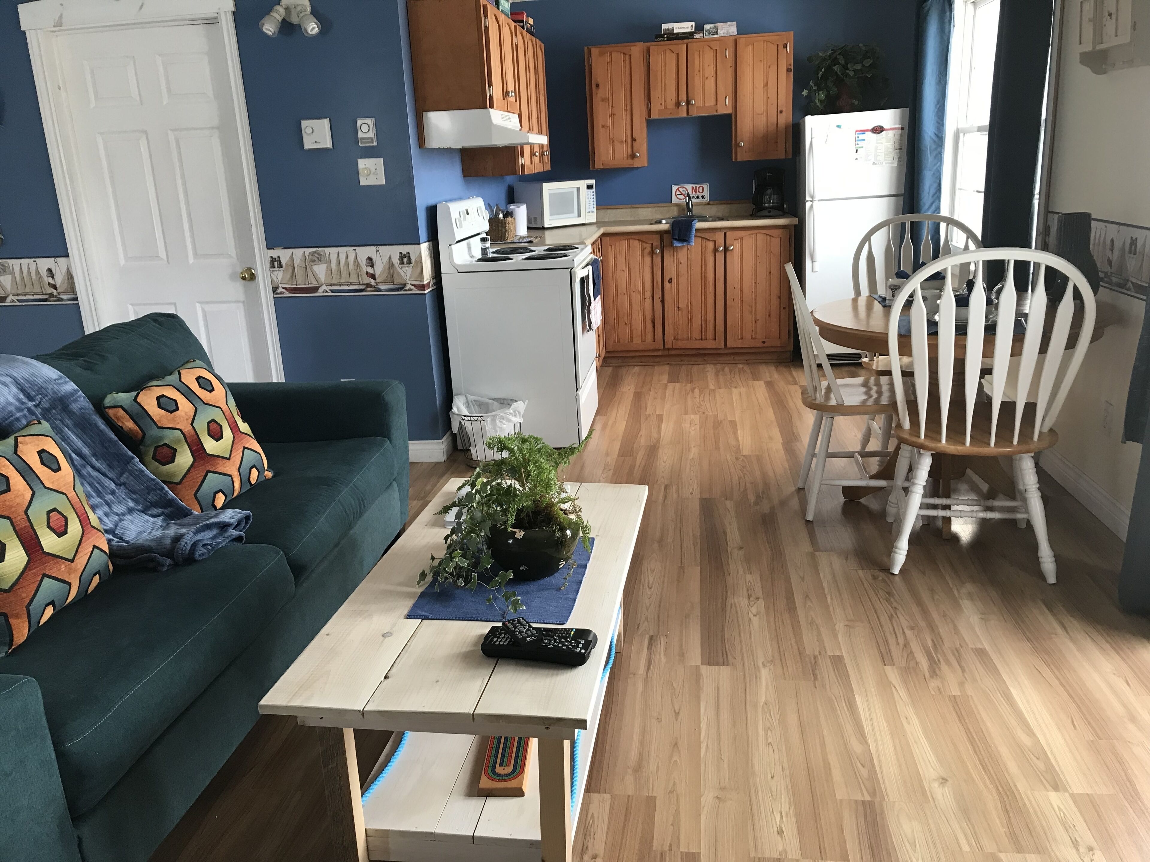 A compact living space with a sofa, a coffee table, a dining table with chairs, a kitchen area with wooden cabinets, a refrigerator, and a microwave.