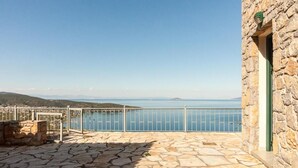 A stone-floored terrace with a stone wall and a metal railing overlooking a body of water. - Epidavros Seascape (Epidaurus)