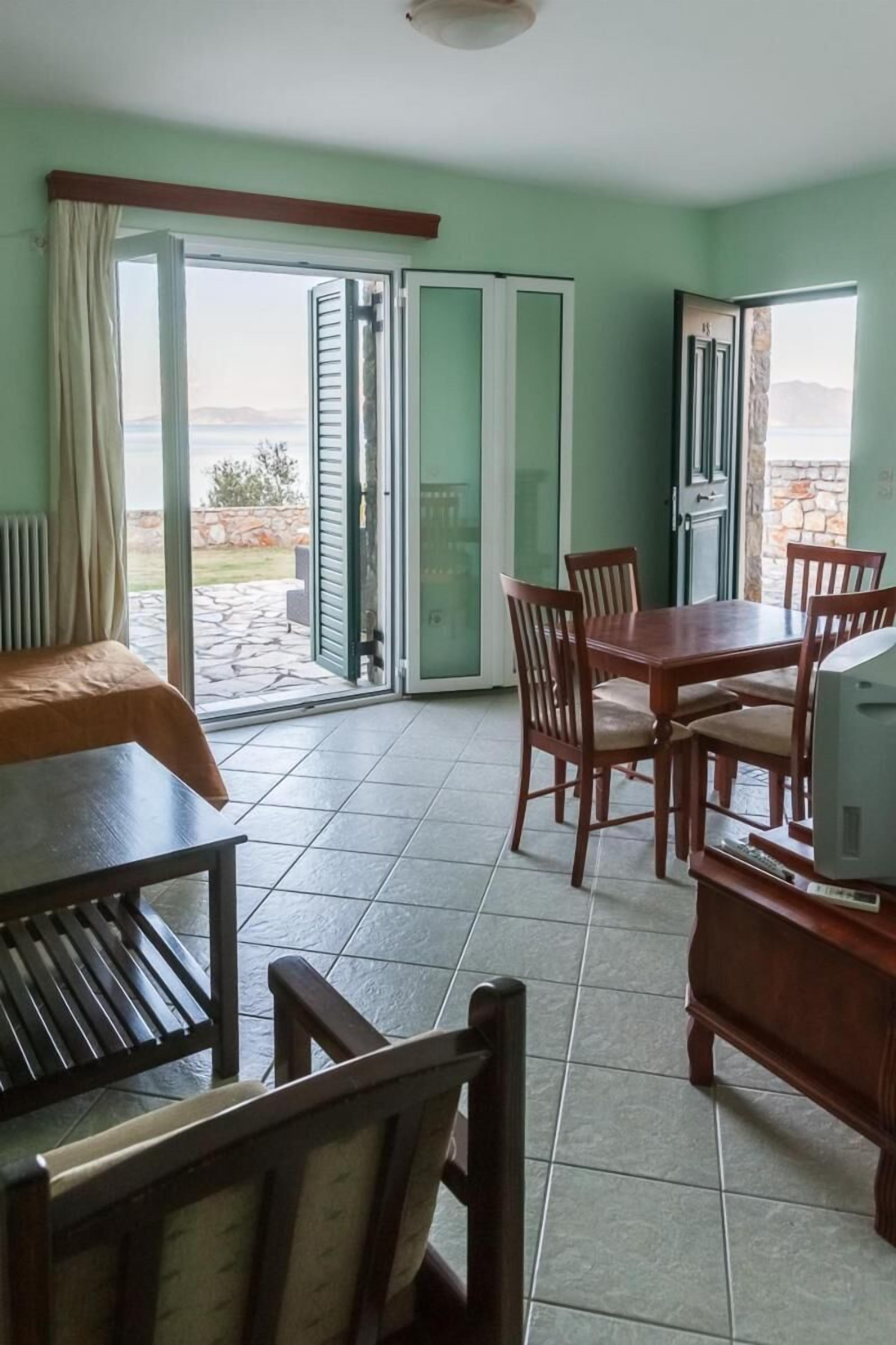 A room with a dining table, chairs, a television, and a view through a sliding glass door.