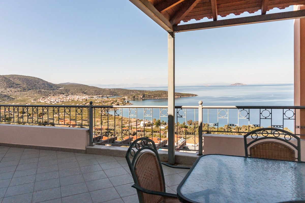 A terrace with a view of the sea and hills, featuring a table and chairs.