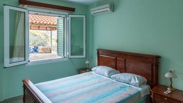 Une chambre à coucher avec un lit, une table de chevet, une fenêtre ouverte et un appareil de climatisation.