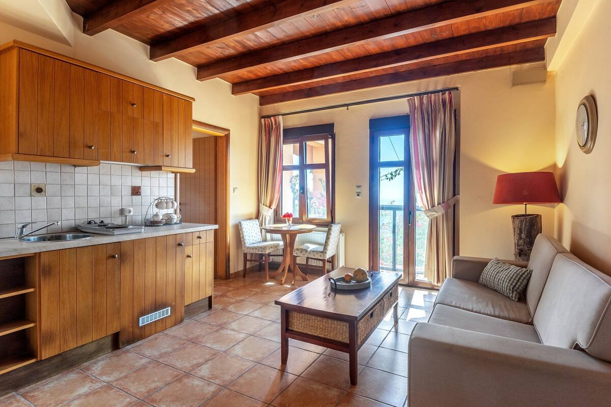 A kitchen with wooden cabinets, a dining area with a table and chairs, and a sofa in a living area.
