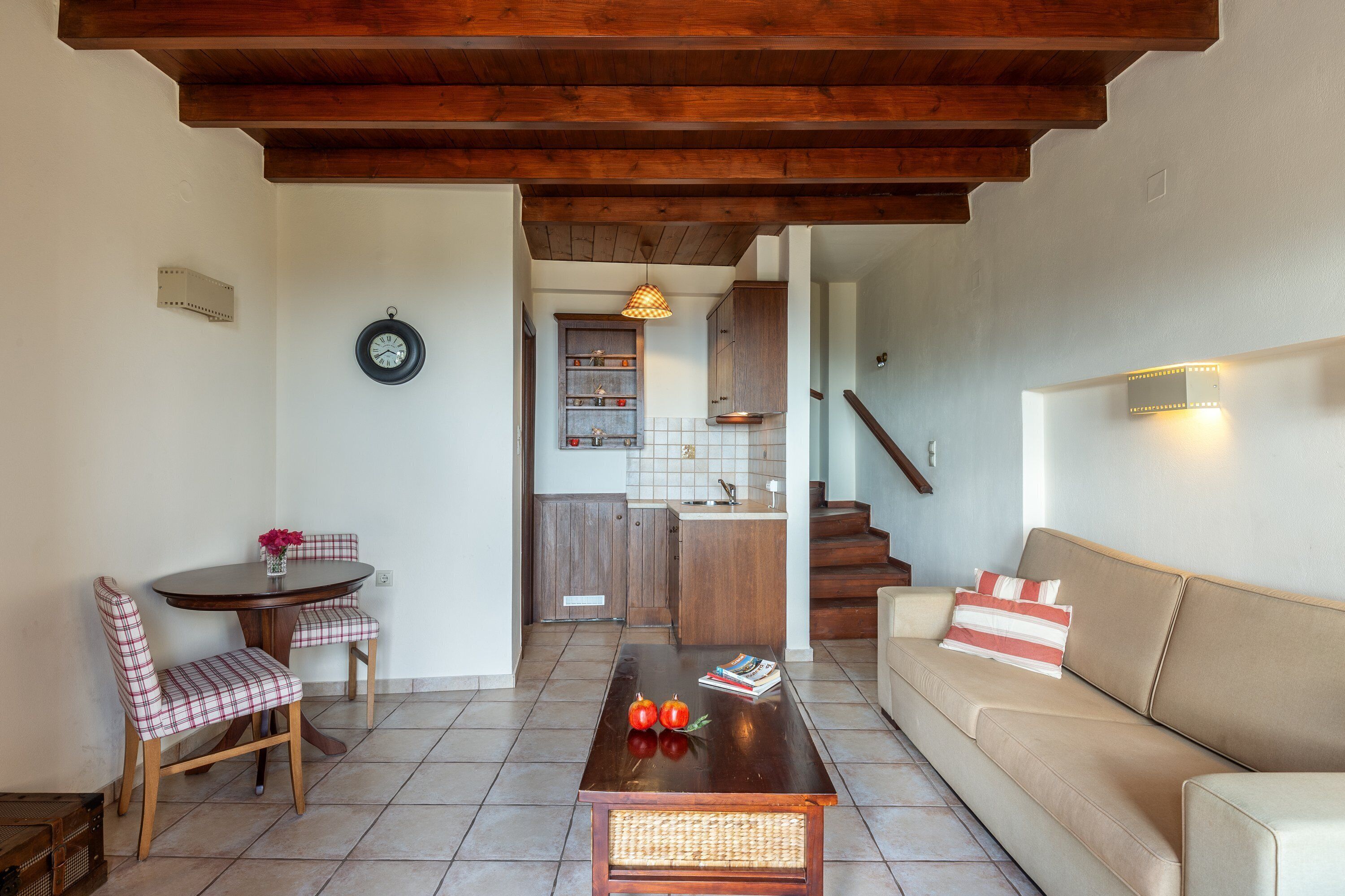 Un salón con techo de madera, una mesa de comedor con sillas, un sofá y una zona de cocina al fondo.