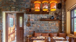 Un comedor con pared de piedra, mobiliario de madera y una mesa dispuesta para dos, con platos, vasos y una jarra.
