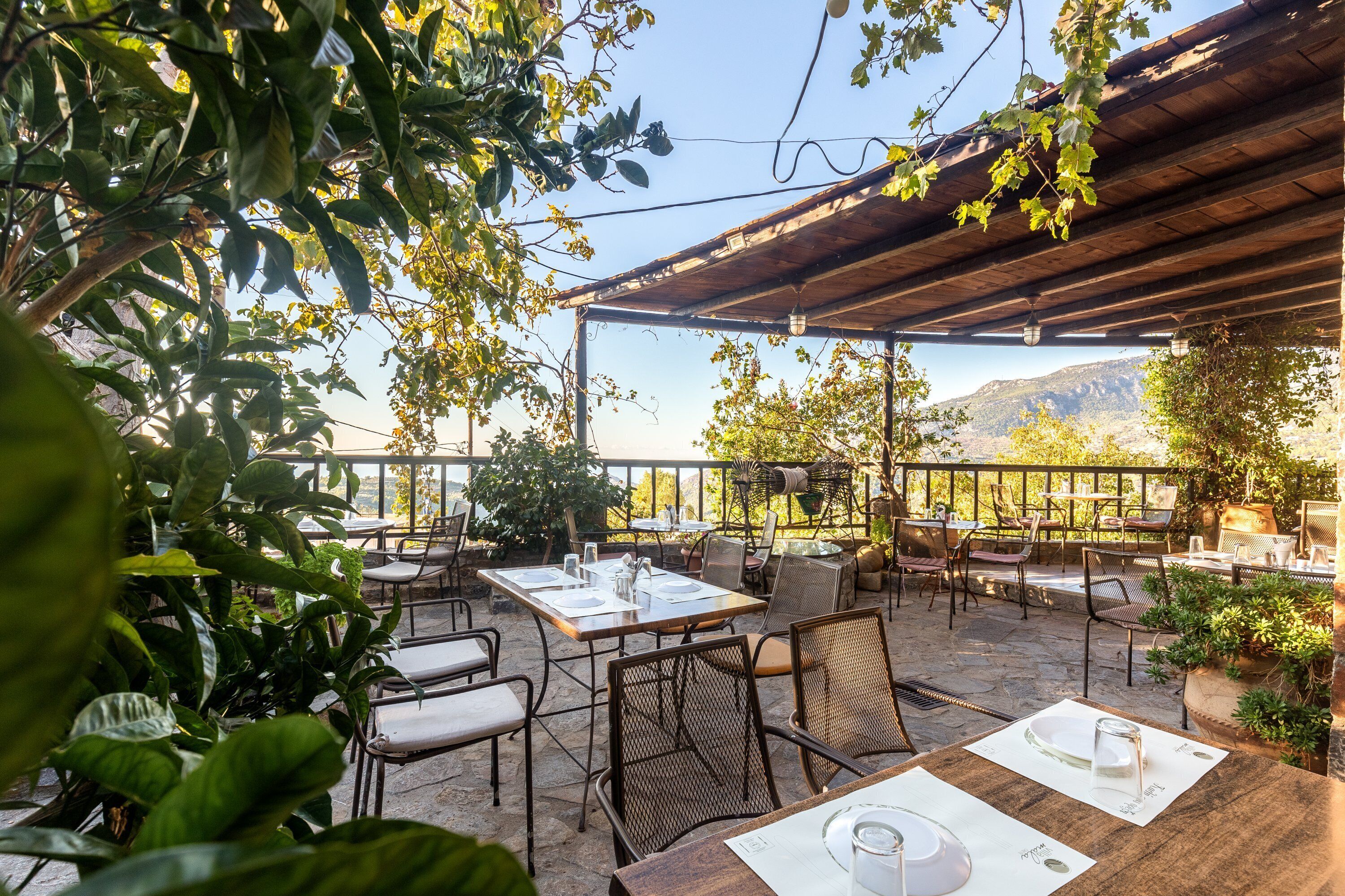 Une terrasse extérieure avec des tables et des chaises, entourée de verdure et offrant une vue sur un paysage montagneux.