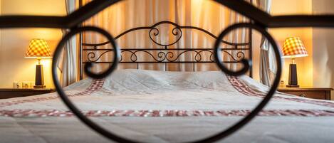 A bed with a metal headboard, two bedside lamps, and a view of a curtain and wall.