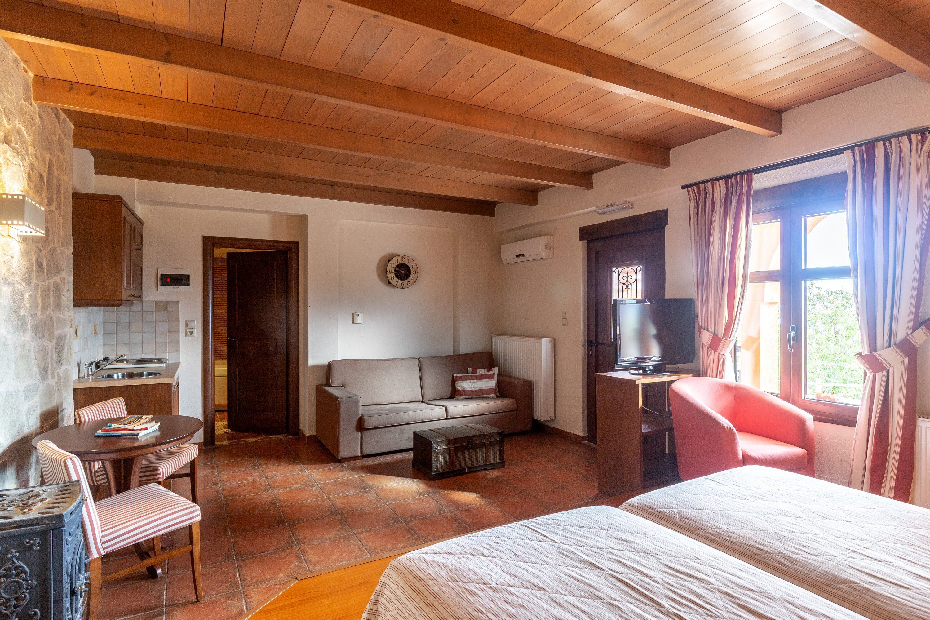 Una habitación acogedora con techo de madera, un sofá, una cama, un televisor y un comedor con mesa y sillas.