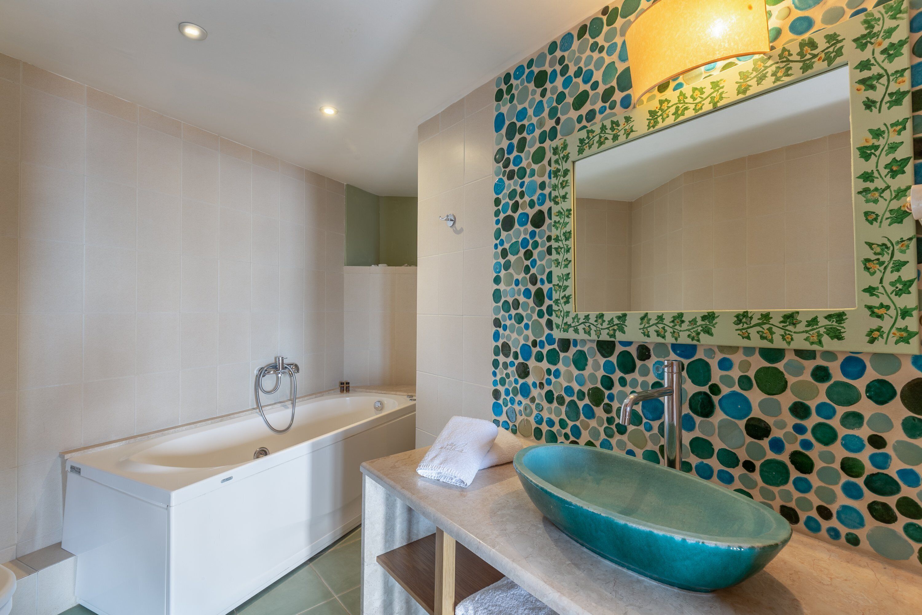 Une salle de bain moderne avec une baignoire, un grand miroir et un mur décoratif en mosaïque.