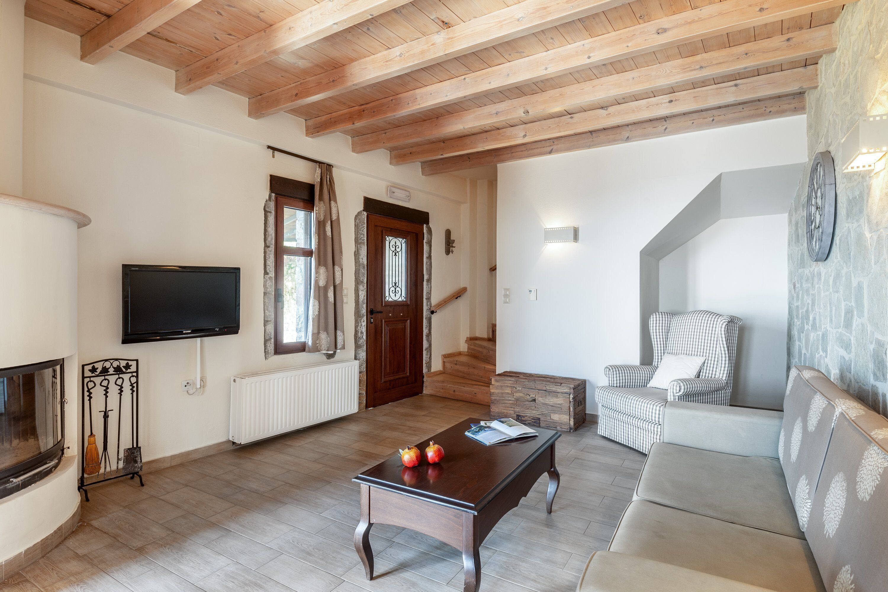 A living room with a wooden ceiling, a TV mounted on the wall, a sofa, a coffee table with apples, and a fireplace.