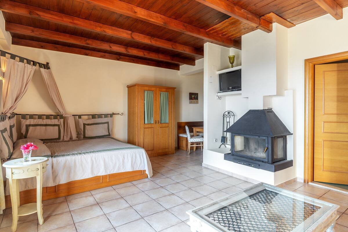 A bedroom with a bed, wooden wardrobe, a small table with a vase, and a fireplace.