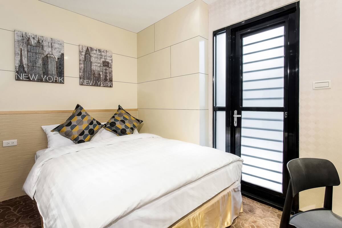 Habitación de hotel con cama, dos obras de arte murales que representan Nueva York, una silla negra y un ventanal corredero.