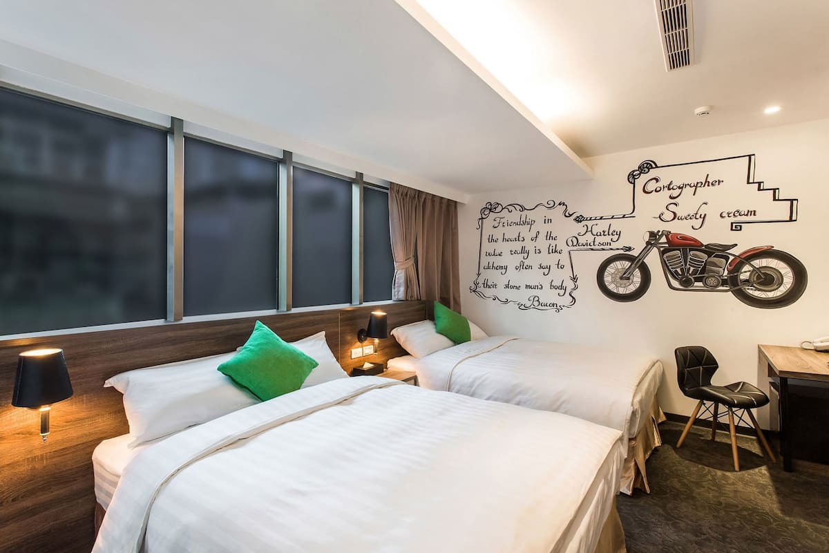 Habitación de hotel con dos camas, un mural en la pared, un escritorio y una silla.