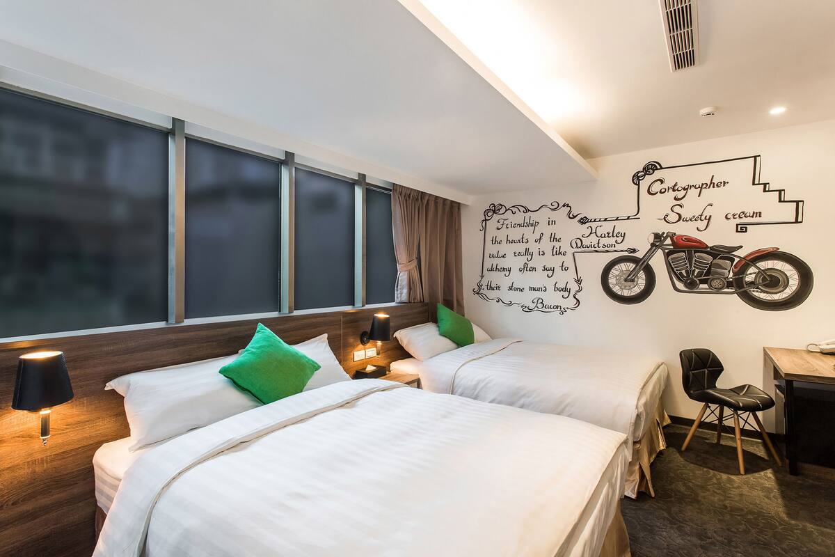 Habitación de hotel con dos camas, un escritorio, una silla y un mural en la pared.