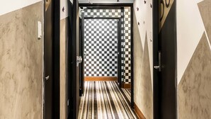 Corredor de hotel com carpete listrado, desenhos geométricos nas paredes e luminárias no teto.