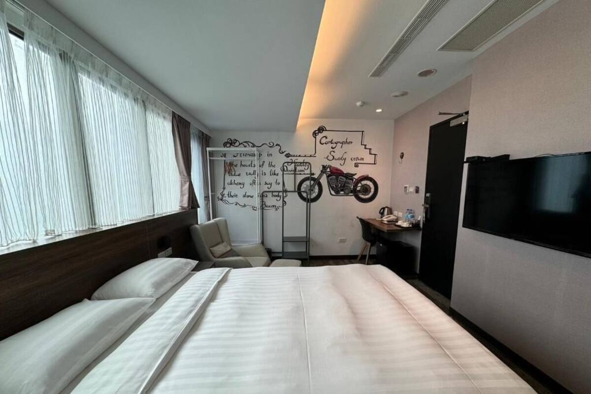 Habitación de hotel con una cama grande, un escritorio, una silla, un televisor y una pared decorada con un adhesivo de motocicleta.