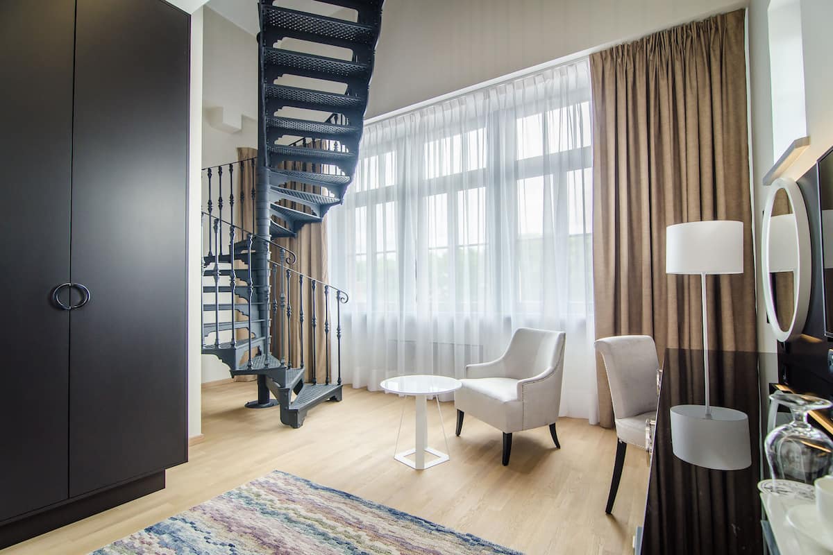 A modern hotel room with a spiral staircase, a round table, two chairs, a large mirror, and a wardrobe.