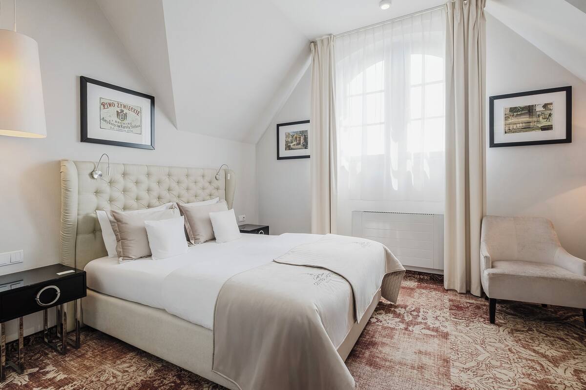 A bedroom with a large bed, a bedside table, a chair, and two framed pictures on the wall.