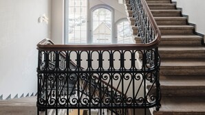 A grand staircase with ornate black railings and a curved design, leading to a second-floor landing with large windows. - Craft Beer Central Hotel (Gdansk)