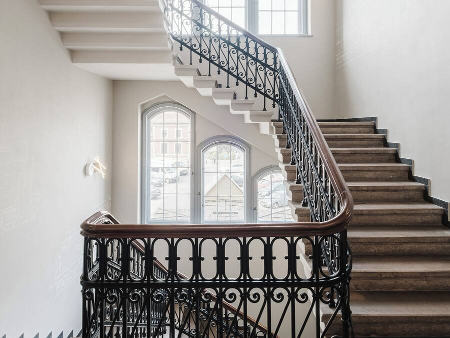 A grand staircase with ornate black railings and a curved design, leading to a second-floor landing with large windows.