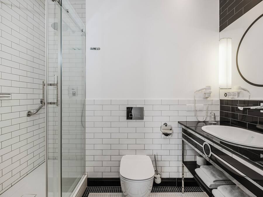 Un baño moderno con cabina de ducha de vidrio, azulejos blancos tipo metro, encimera negra y lavamanos blanco.