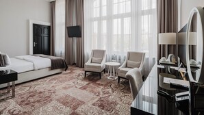 A hotel room with a bed, two armchairs, a small table, a desk with a mirror, and a large window with curtains. - Craft Beer Central Hotel (Gdansk)