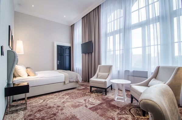 A hotel room with a bed, two armchairs, a small table, a TV, and a large window with curtains. - Craft Beer Central Hotel (Gdansk)