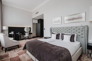 Quarto de hotel com uma cama grande, uma escrivaninha com cadeira, um espelho e duas molduras na parede.