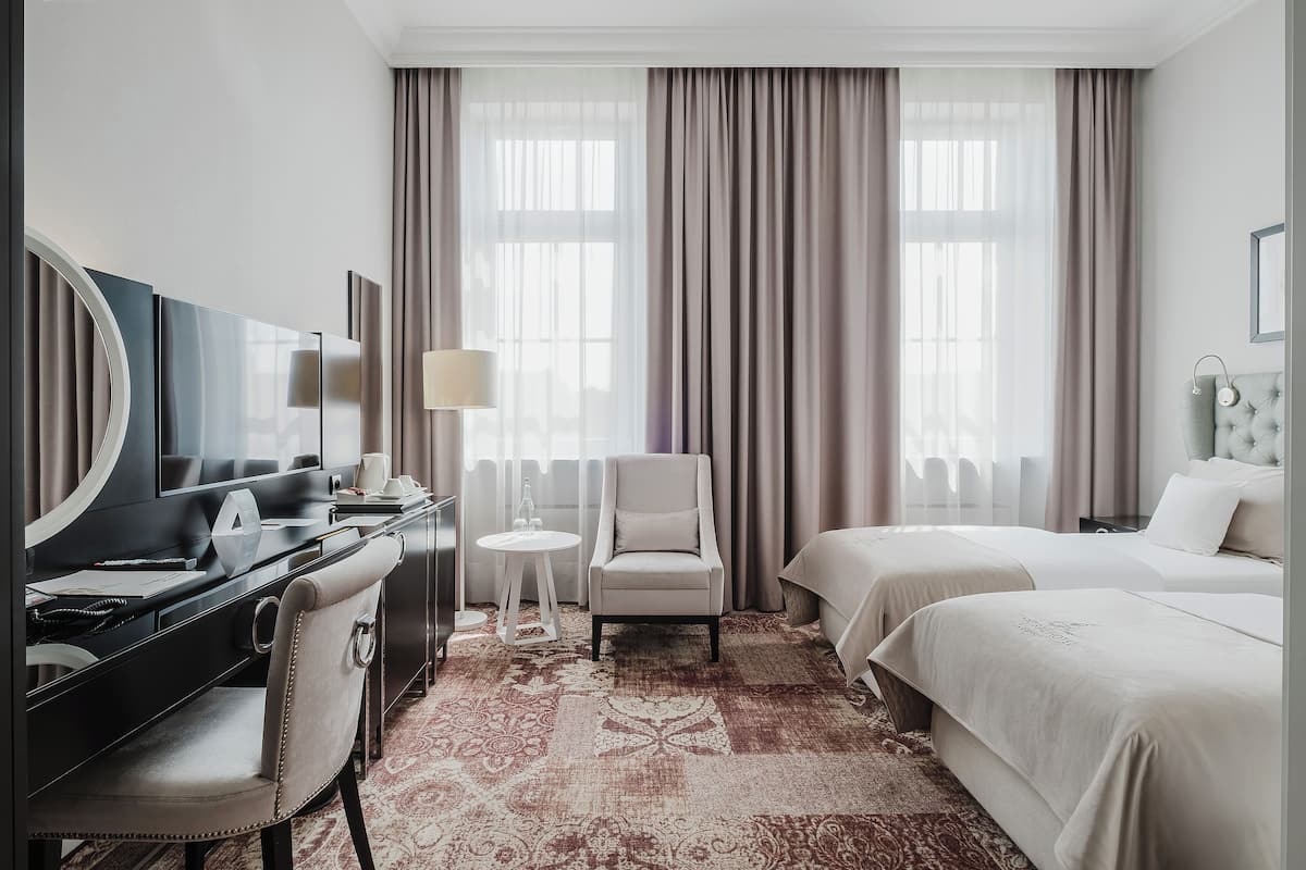A hotel room with a large bed, a smaller bed, a desk with a chair, a TV, and a large window with curtains.