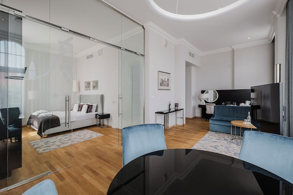 Una habitación de hotel moderna con separador de vidrio, una cama, un sofá, un televisor y una pequeña mesa.