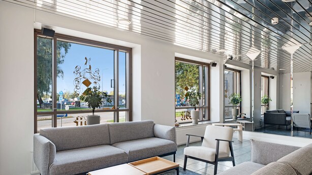 A modern interior with a grey sofa, a white armchair, and a coffee table. Large windows offer views of the outside. - Summer Hotel Tott (Savonlinna)