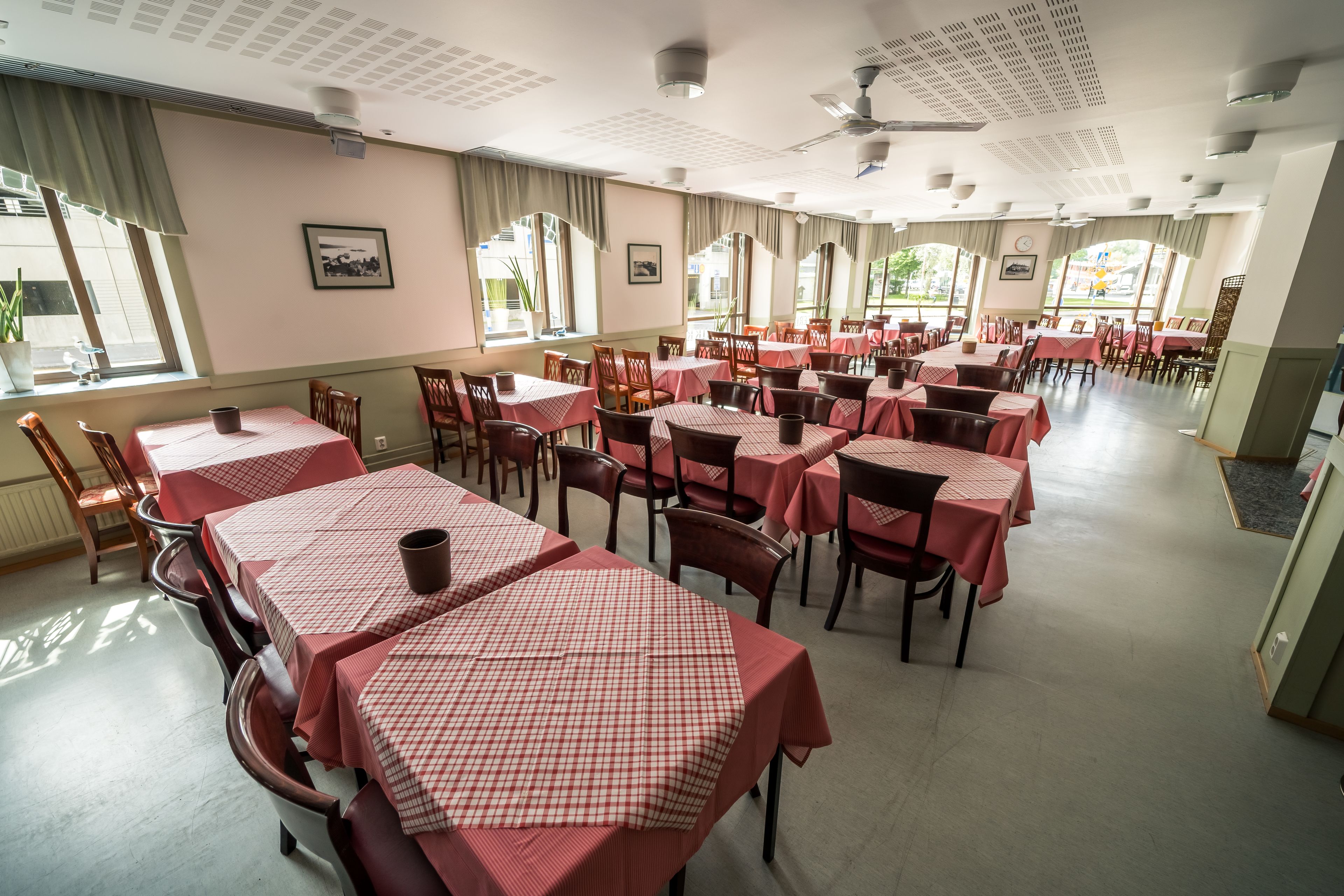 Un restaurante amplio con varias mesas cubiertas de manteles a cuadros rojos, dispuestas en filas con sillas.