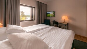 A hotel room with two beds, a desk, a lamp, a TV, and a window with curtains. - Summer Hotel Tott (Savonlinna)