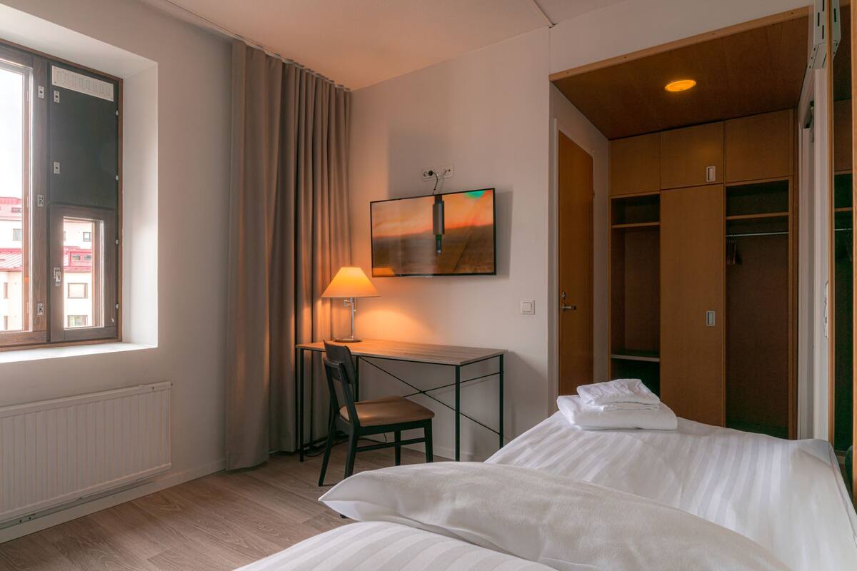 A hotel room with a bed, a desk with a chair, a TV, and a wardrobe.