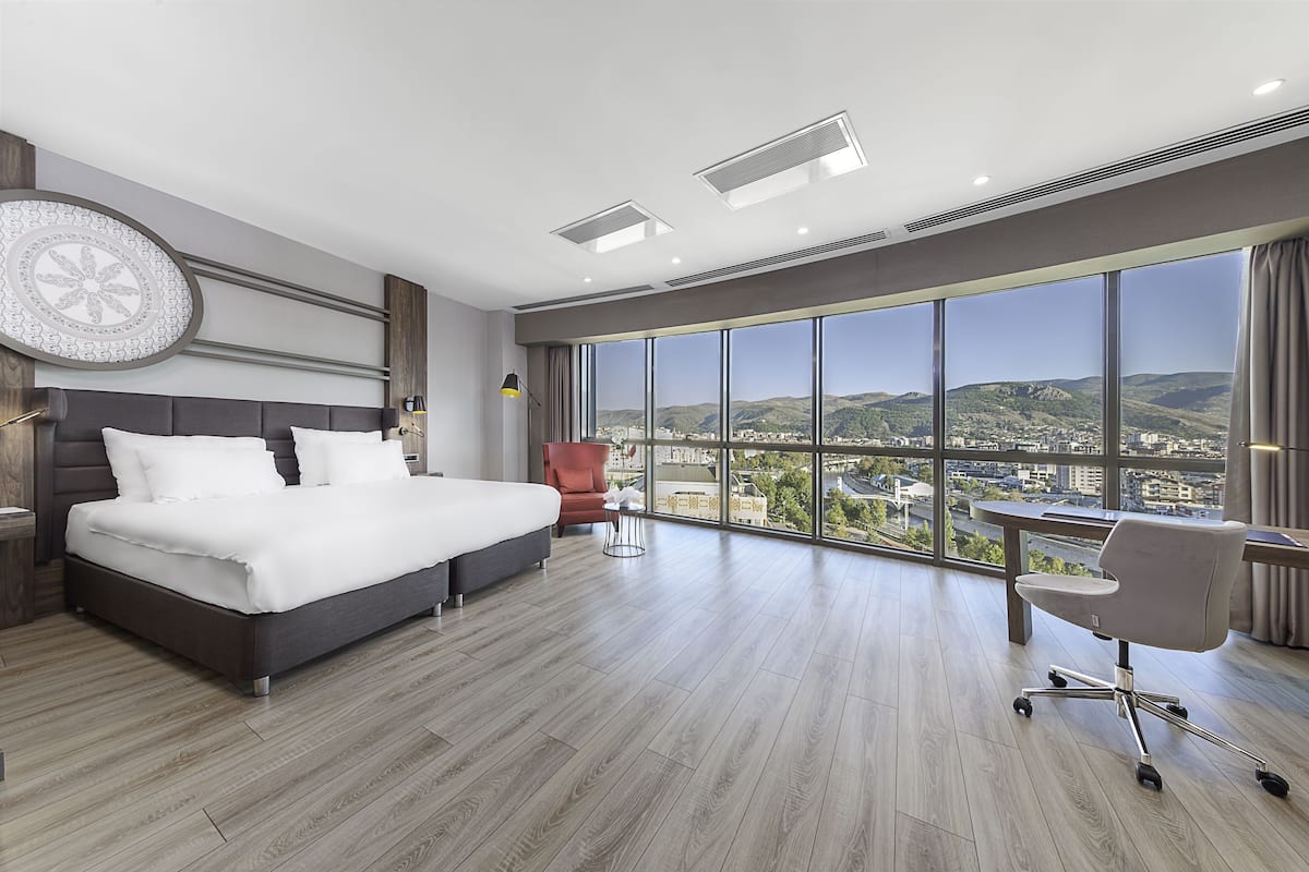 Ein modernes Hotelzimmer mit einem großen Bett, einem Schreibtisch und Blick auf die Stadt.