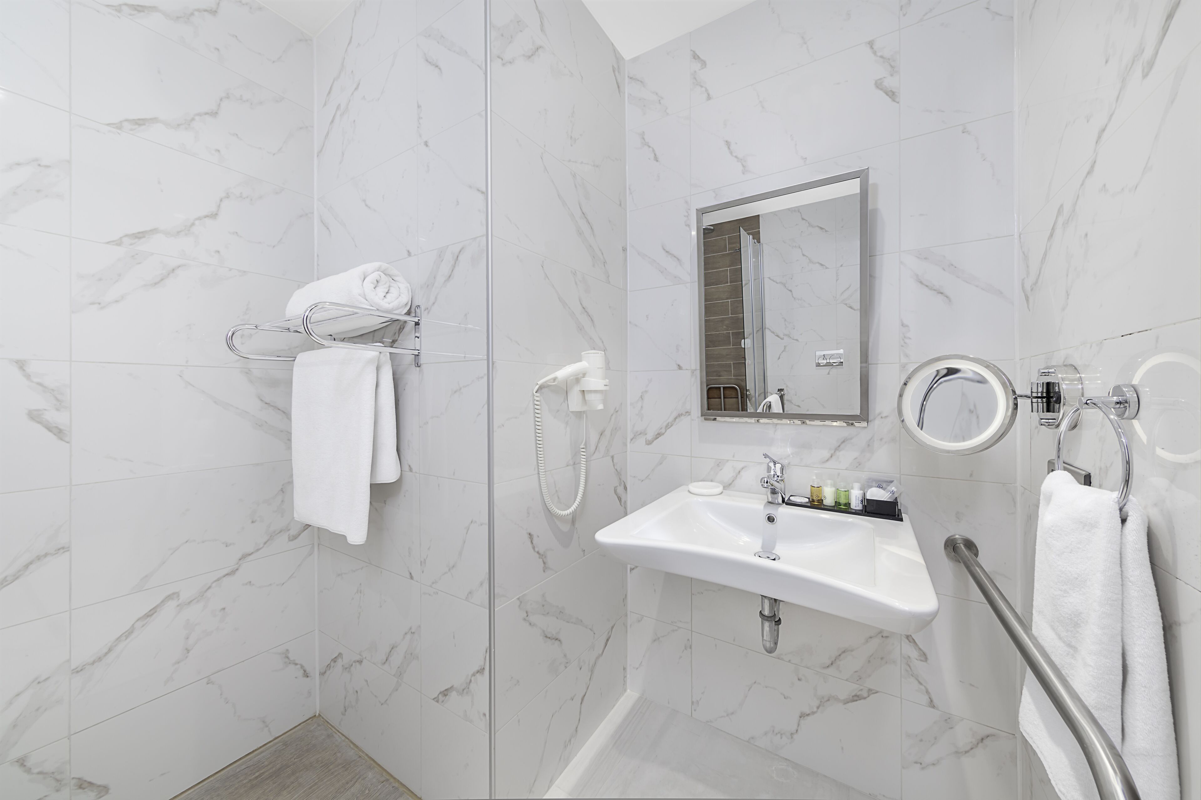 Ein modernes Badezimmer mit Marmorboden, einem weißen Waschbecken, einem Spiegel und einer Handbrause.
