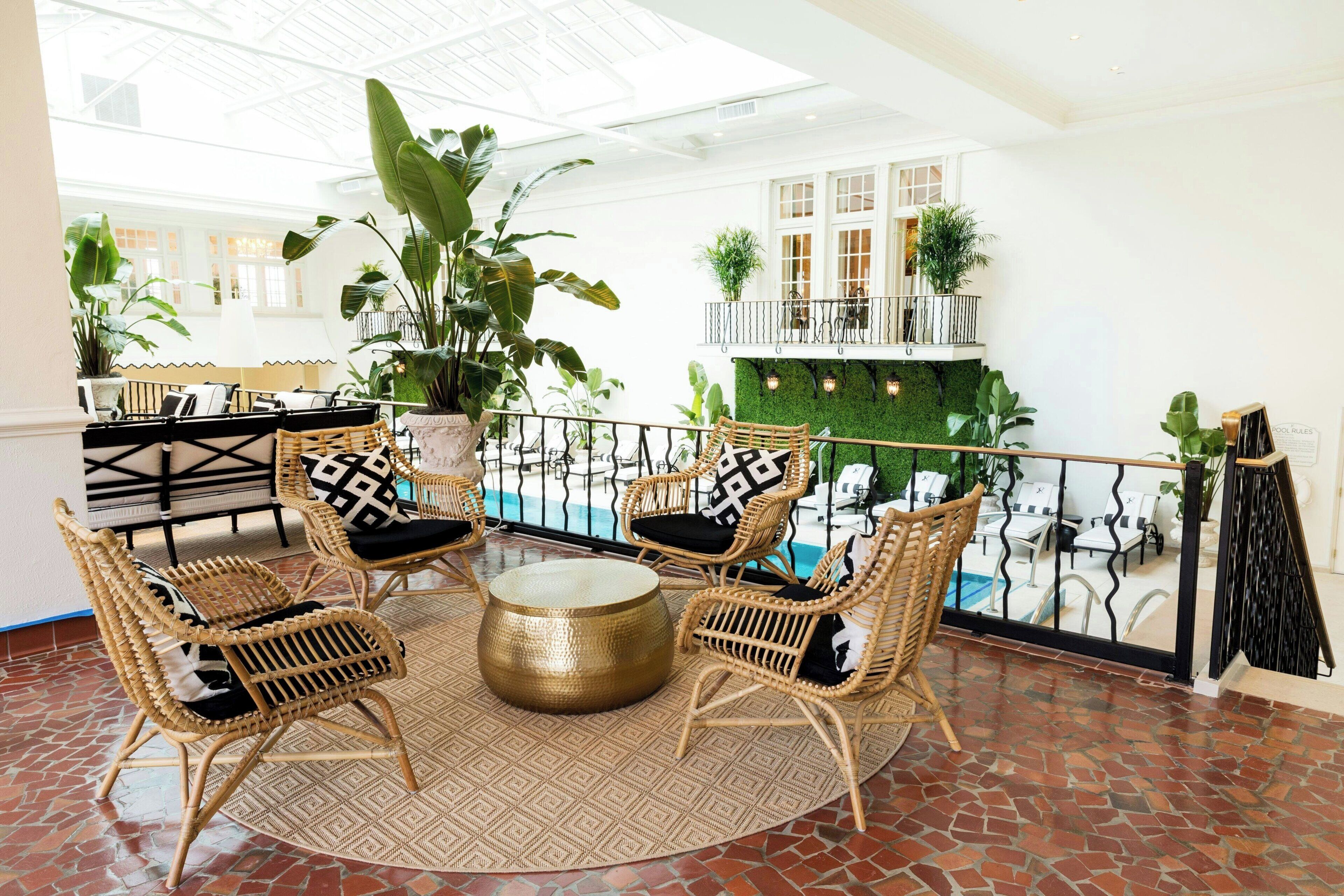 A spacious balcony with wicker furniture, a round table, and a view of a pool and greenery.