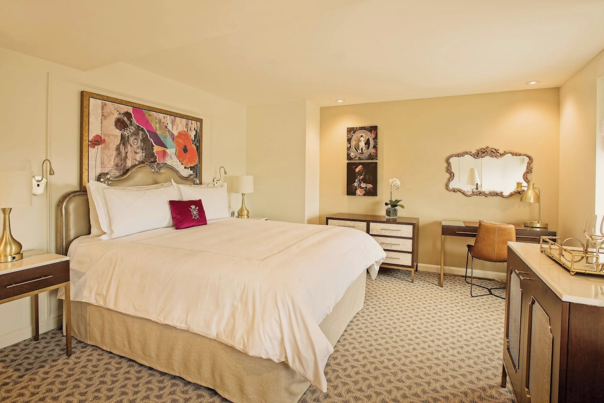 A hotel room with a large bed, a desk, a chair, and a dresser.