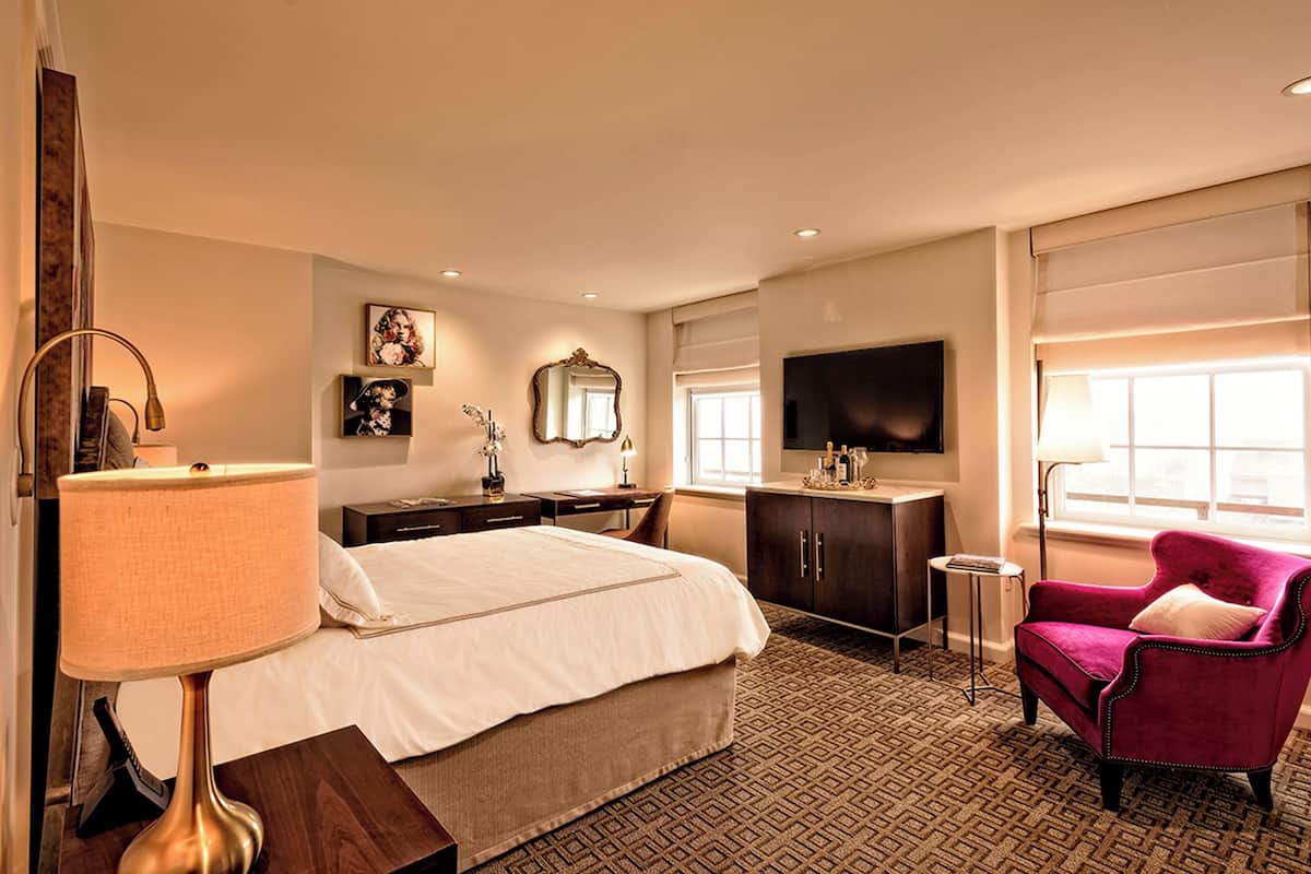 A hotel room with a bed, a desk, a chair, a TV, and a window.