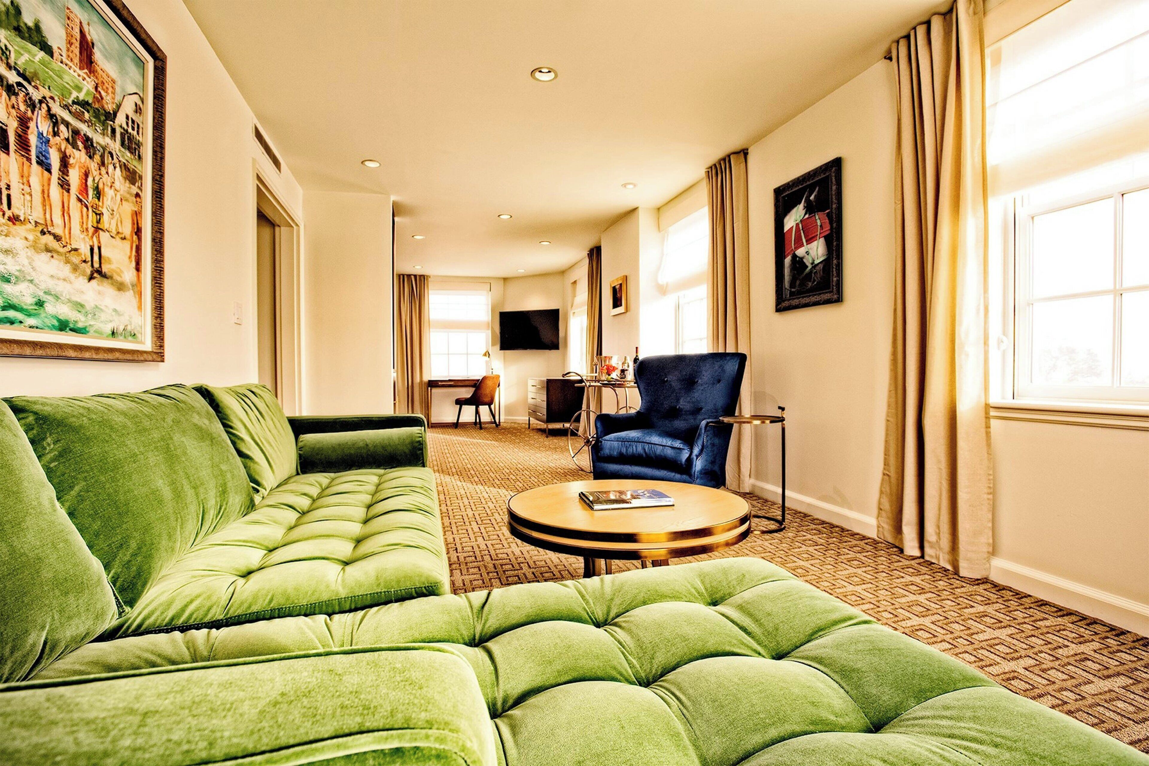 Une chambre d’hôtel avec un canapé vert, une table basse ronde et un téléviseur fixé au mur.