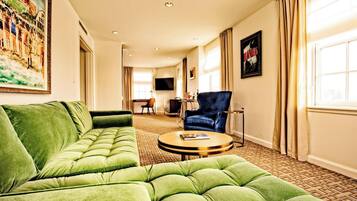 Une chambre d’hôtel avec un canapé vert, une table basse ronde et un téléviseur fixé au mur.