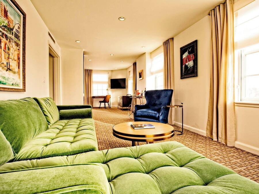 Une chambre d’hôtel avec un canapé vert, une table basse ronde et un téléviseur fixé au mur.