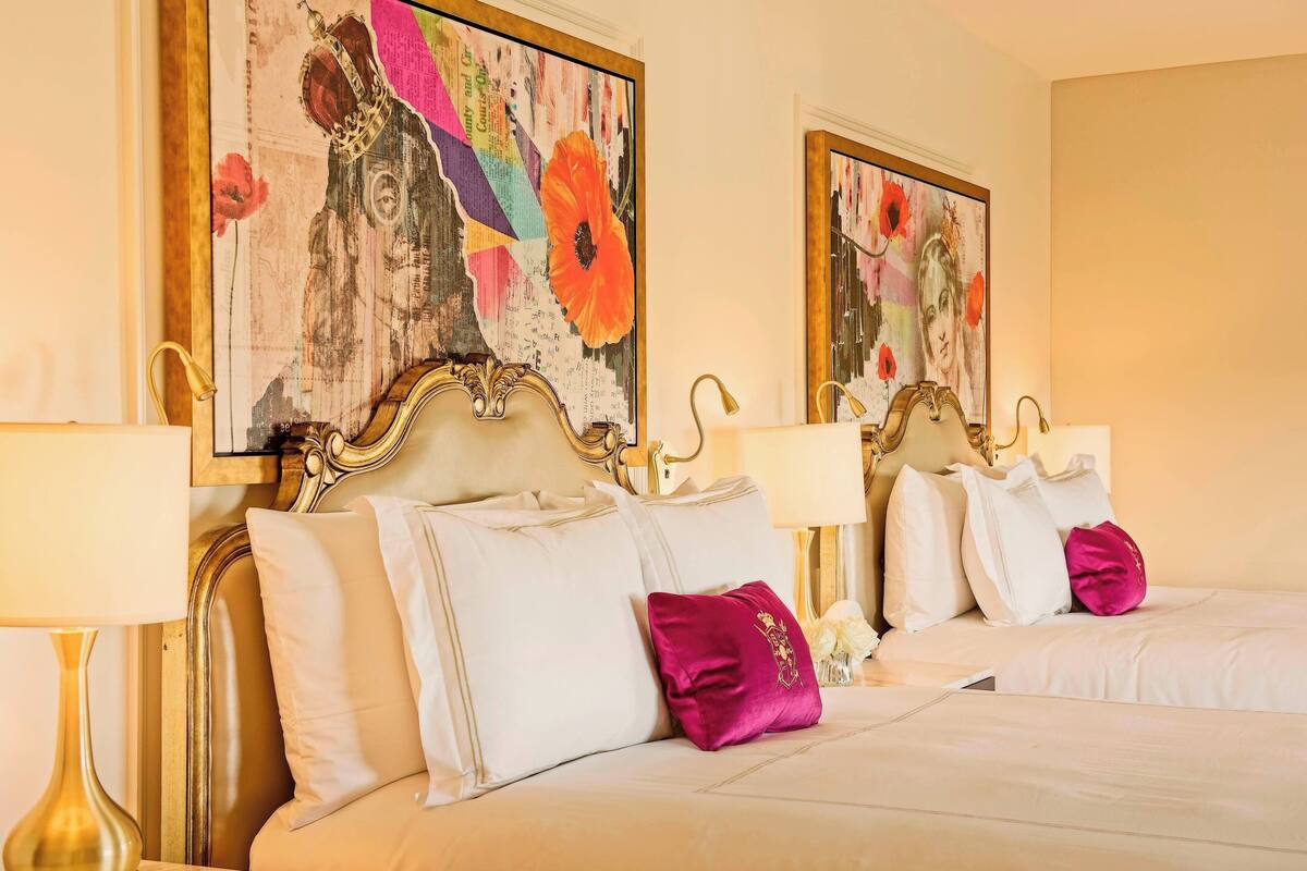 A hotel room with two beds, each with a headboard, white bedding, and a single decorative pillow.