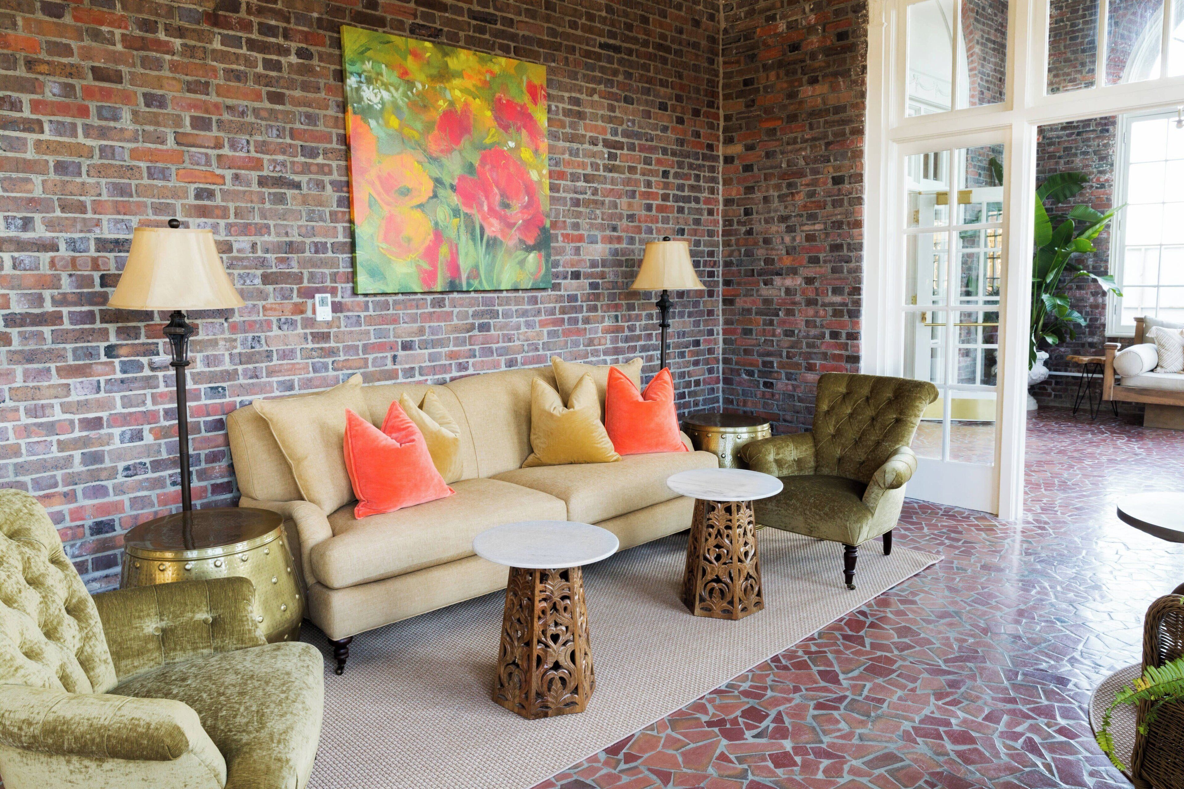 A cozy lounge area with a brick wall, a sofa with cushions, two side tables, and a chair.