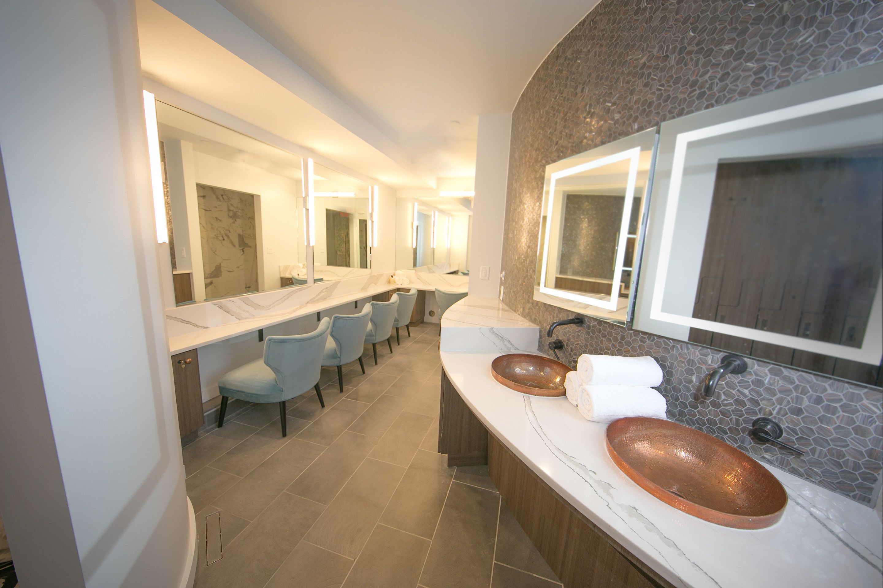 Une salle de bain moderne avec deux lavabos, un grand miroir et un coin salon avec des chaises.