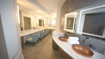 Une salle de bain moderne avec deux lavabos, un grand miroir et un coin salon avec des chaises.