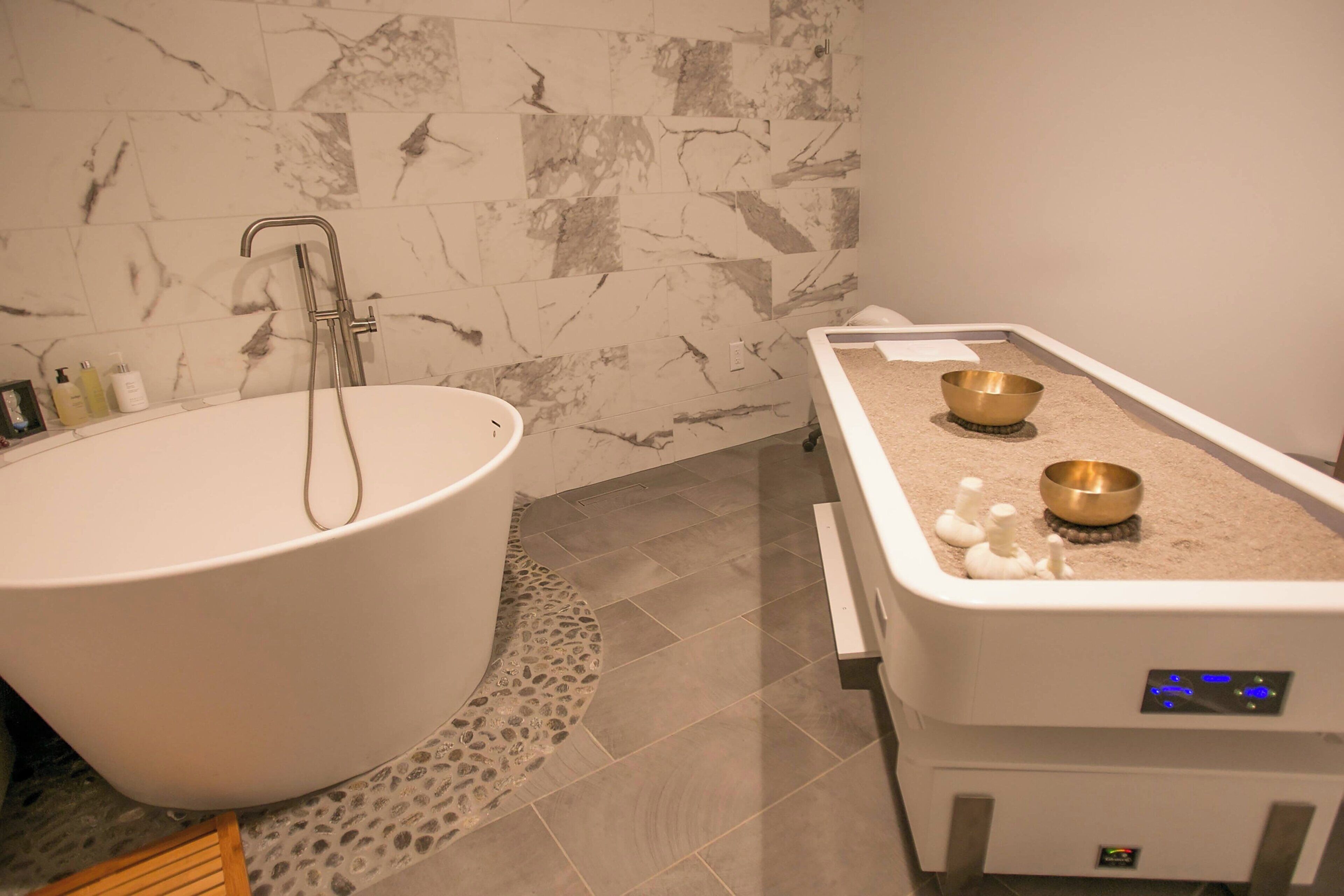 A modern bathroom with a freestanding bathtub, a massage table, and a small altar with bowls.