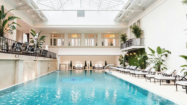 An indoor swimming pool with a glass ceiling, lounge chairs, and potted plants. - The Historic Cavalier Hotel and Beach Club, Autograph Collection (Virginia Beach)