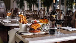A dining table set with a burger, fries, a bottle of wine, and glasses. - The Historic Cavalier Hotel and Beach Club, Autograph Collection (Virginia Beach)