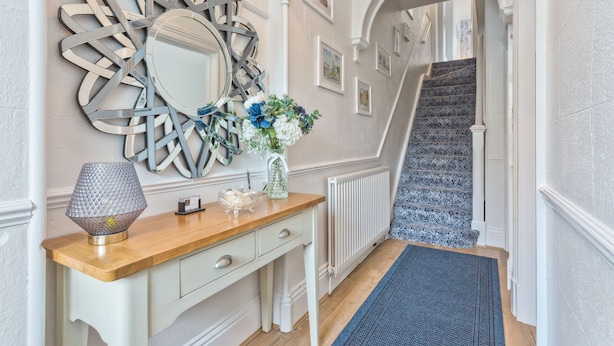 Un couloir avec une console en bois, un miroir décoratif et un vase rempli de fleurs.