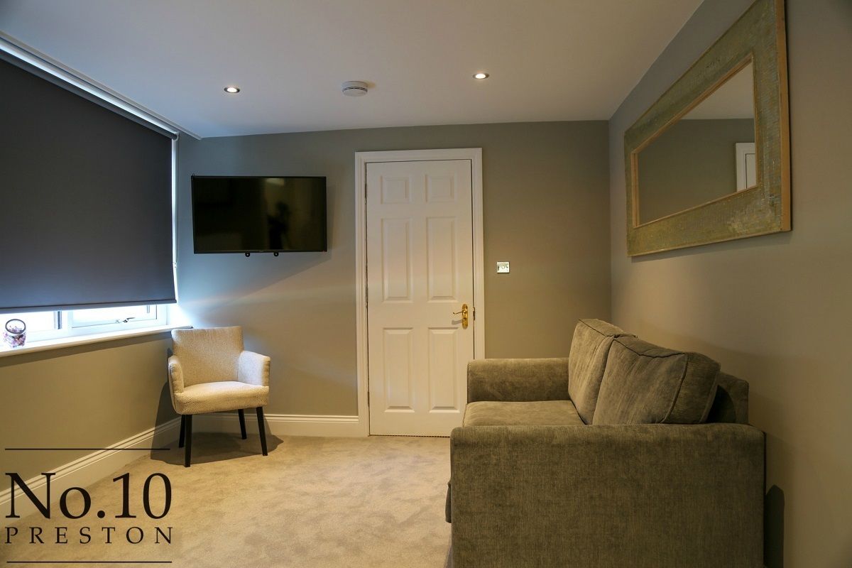 A room with a beige carpet, a white door, a television mounted on the wall, and a large mirror.